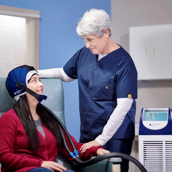 Nurse smiles are patient wearing a blue scalp cooling cap