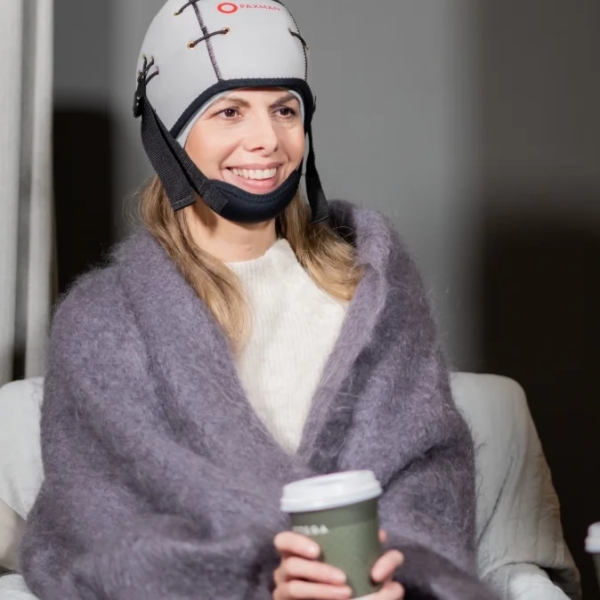 Patient smiles while wearing a gray scalp cooling cap and holding a hot beverage